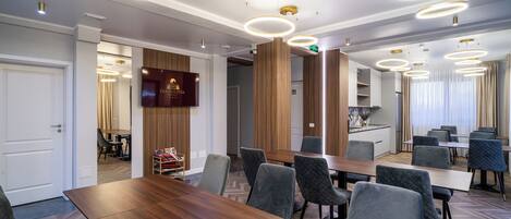 A modern conference room with a long wooden table, multiple grey upholstered chairs, and circular ceiling lights.