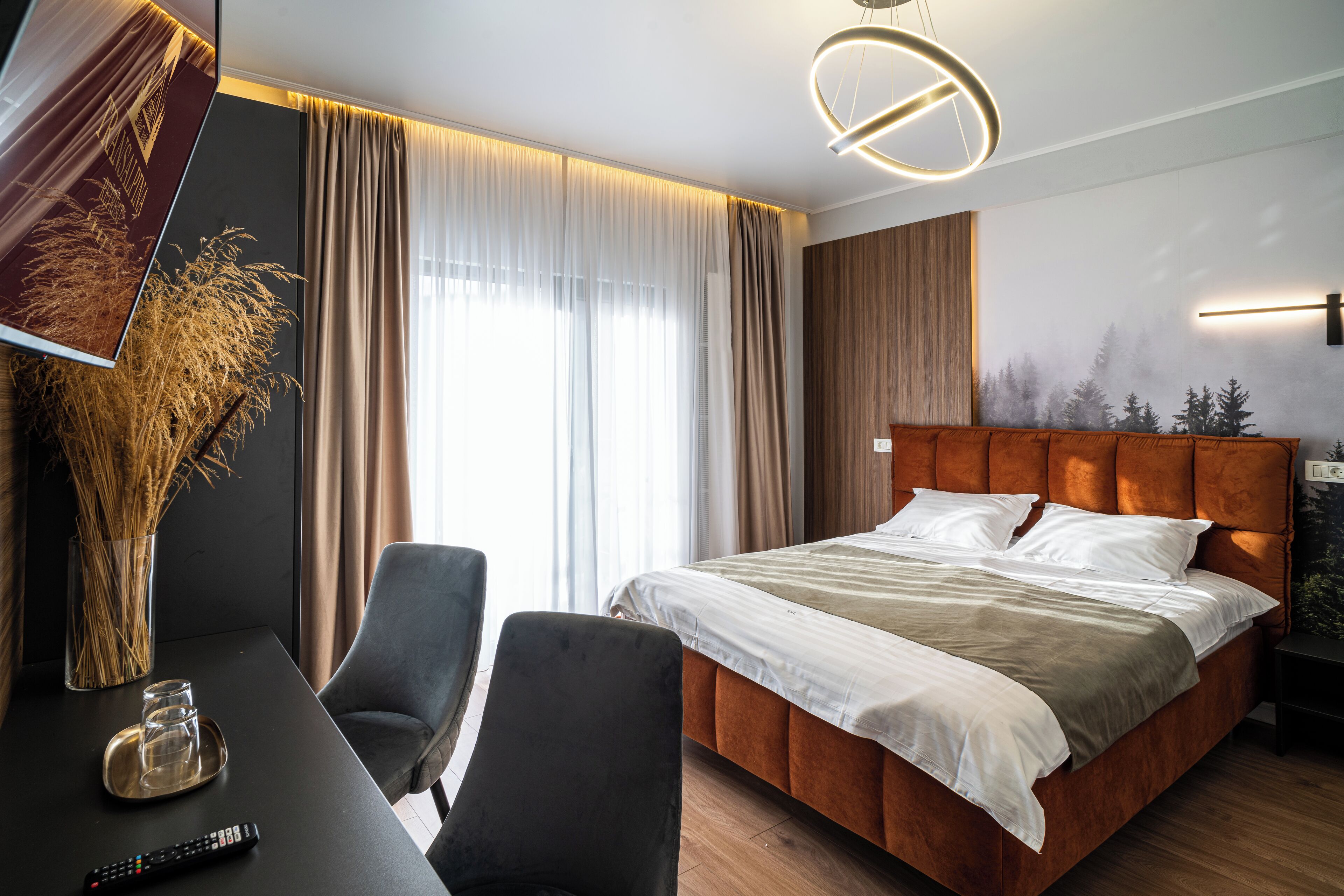 Una moderna camera d'albergo con un letto grande, una scrivania con una sedia, una televisione e un'ampia finestra con tende.