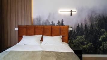 A bedroom with a large bed, a headboard, a nightstand, and a wall mural of a forest.