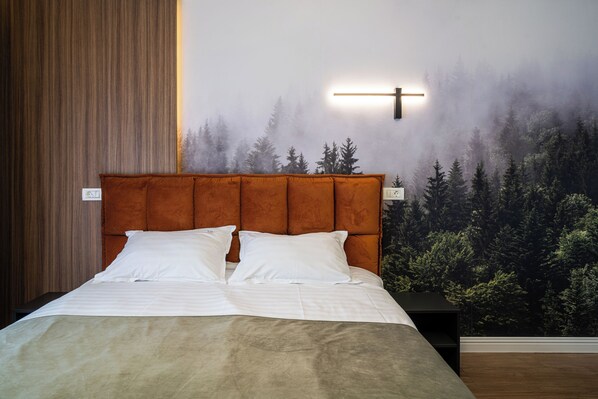 A bedroom with a large bed, a headboard, a nightstand, and a wall mural of a forest.