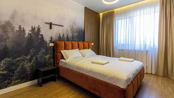 A bedroom with a large bed, a nightstand, a wall mural, and a window with curtains.