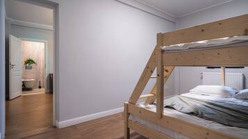 Una habitación con una cama litera, suelo de madera, una puerta blanca que da al baño y un radiador en la pared.