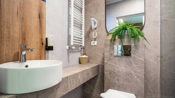 A modern bathroom with a white sink, a towel rack, a hanging plant, and a mirror.