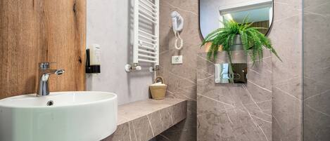 A modern bathroom with a white sink, a towel rack, a hanging plant, and a mirror.
