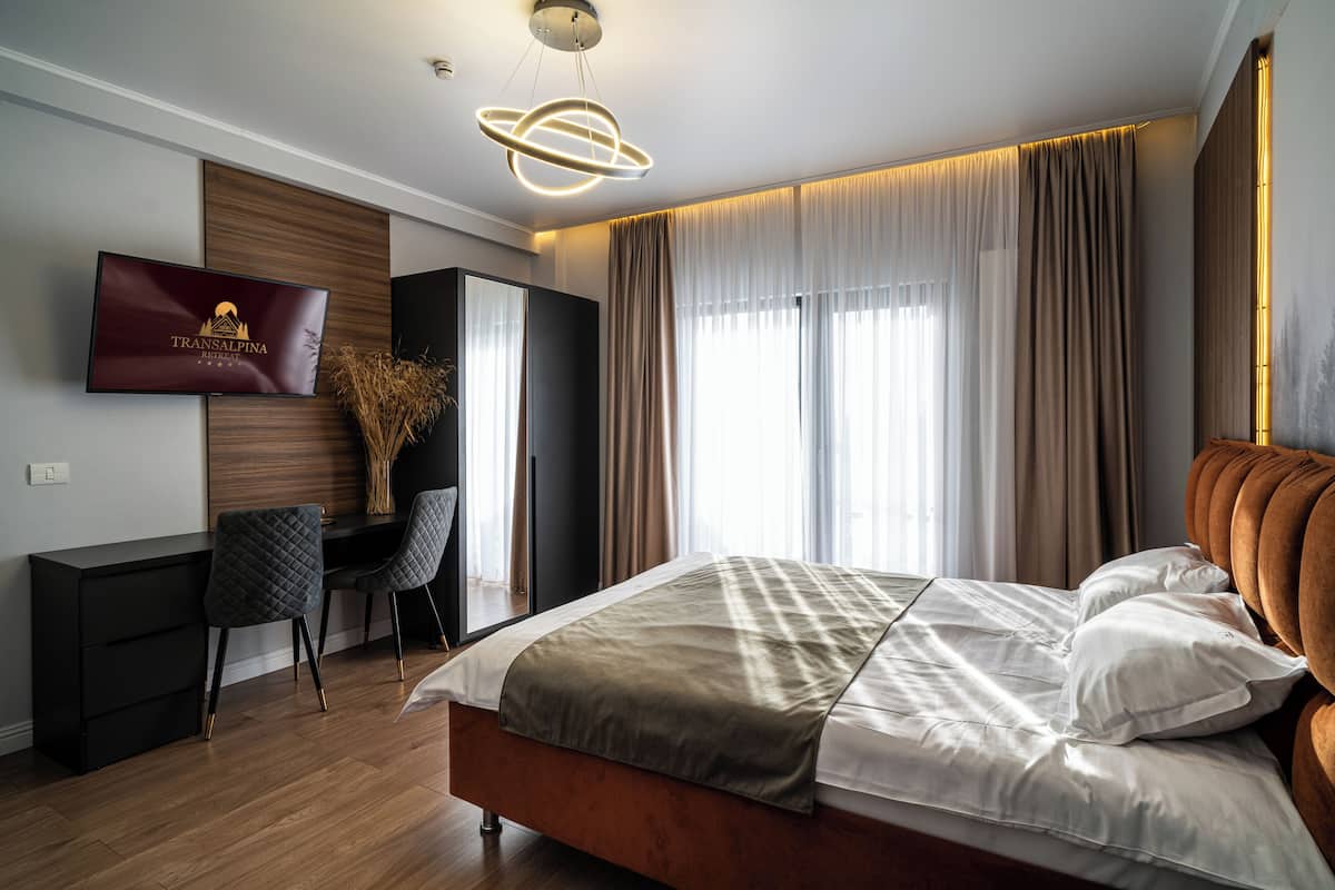 A modern hotel room with a bed, a desk, and a TV mounted on the wall.