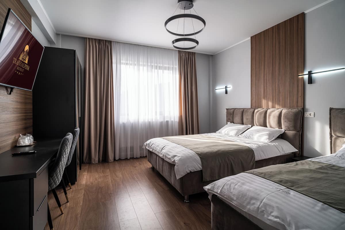 A modern hotel room with a wooden floor, a large bed with a headboard, a desk with a chair, and a television.