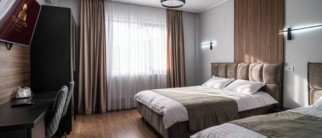 A modern hotel room with a wooden floor, a large bed with a headboard, a desk with a chair, and a television.