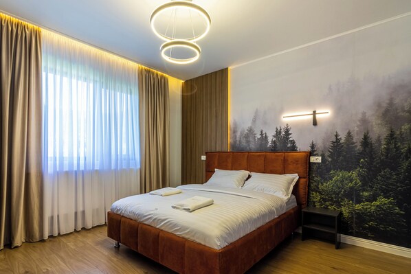 Un dormitorio con cama de madera, una mesita de noche, un mural en la pared de un bosque y una lámpara del techo.