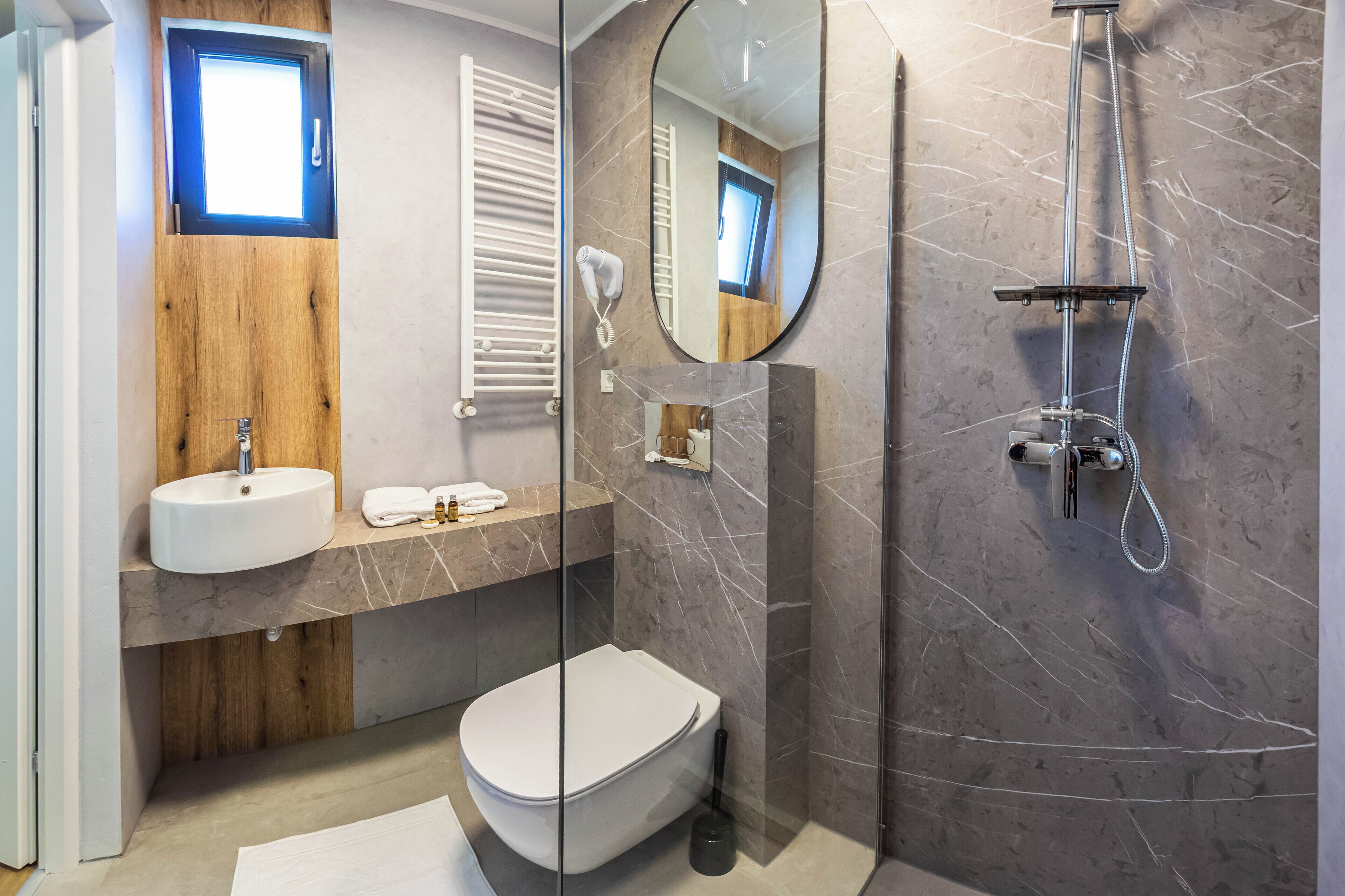 A modern bathroom with a wooden vanity, a white sink, a toilet, and a glass-enclosed shower.