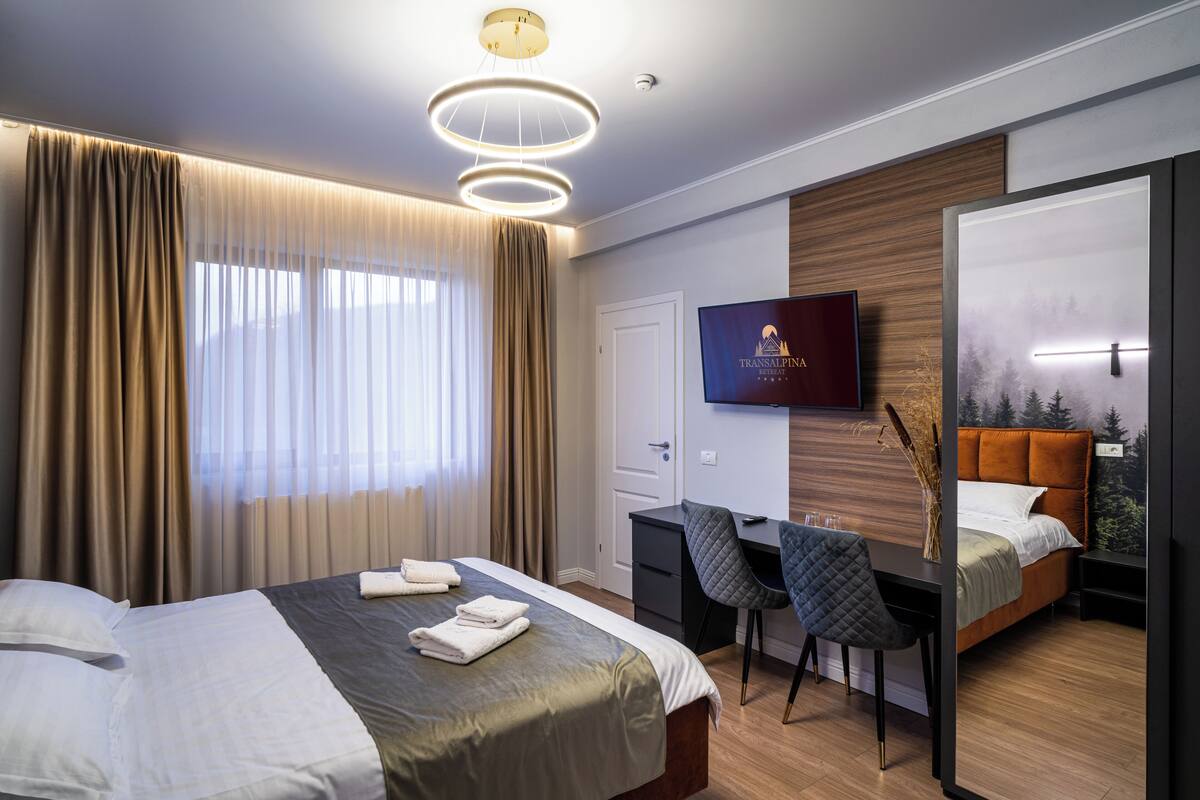 A modern hotel room with a bed, a desk, a chair, and a TV.