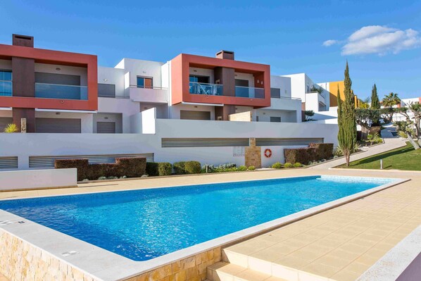 A modern building with a swimming pool, featuring balconies and a clear sky.