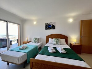 A hotel room with two beds, a balcony, and a painting on the wall. - Monte Gordo Beach Ocean View 3 by Homing (Vila Real Santo Antonio)