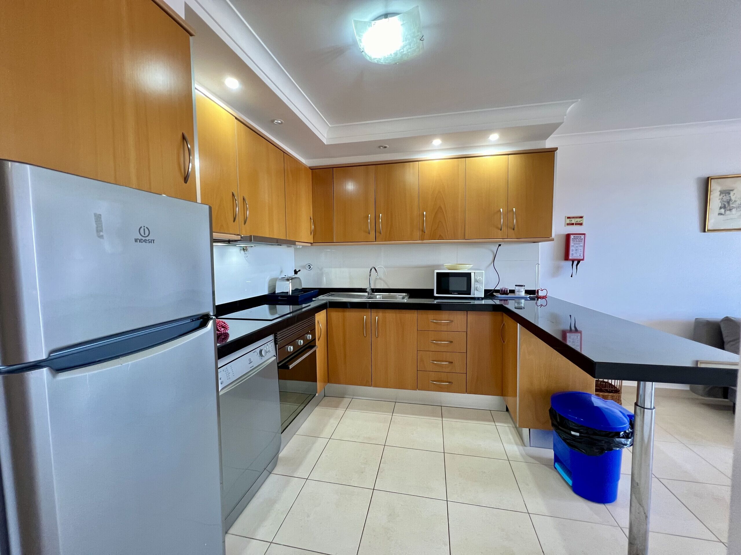 Una cocina con armarios de madera, un refrigerador de acero inoxidable, un microondas y un lavamanos.