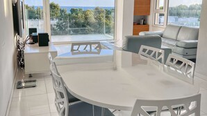 A modern conference room with a large table and white chairs, large windows with a view of the sea, and a sofa in the background. - Modern seafront apartment (Limassol)