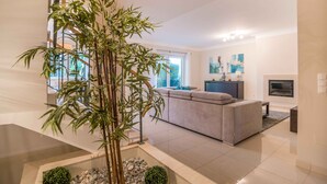 A modern living room with a large bamboo plant, a grey sofa, and a fireplace. - Portimão Elegant House by Homing (Portimão)