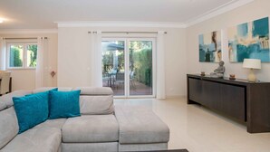 A modern living room with a grey sectional sofa, a dark coffee table, and a large sliding glass door leading to an outdoor patio. - Portimão Elegant House by Homing (Portimão)