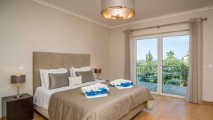 A spacious bedroom with a large bed, a nightstand with a lamp, and a balcony with outdoor furniture. - Portimão Elegant House by Homing (Portimão)