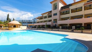 A large swimming pool with a tiled deck, surrounded by multi-story buildings with balconies and a small pavilion.