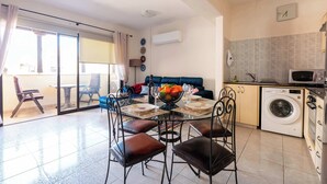 A modern kitchen with a washing machine, a dining table with chairs, and a blue sofa.