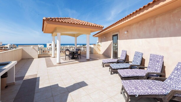 A rooftop terrace with lounge chairs, a table, and a covered seating area overlooking the sea.
