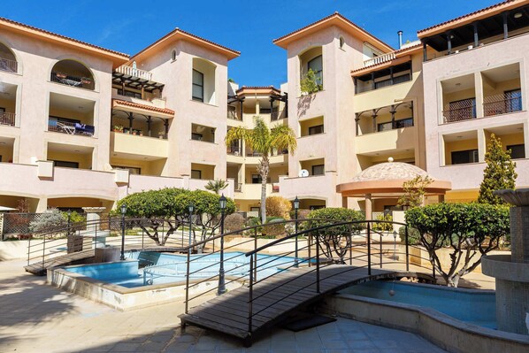 A multi-story hotel with balconies, a swimming pool, and a wooden bridge.