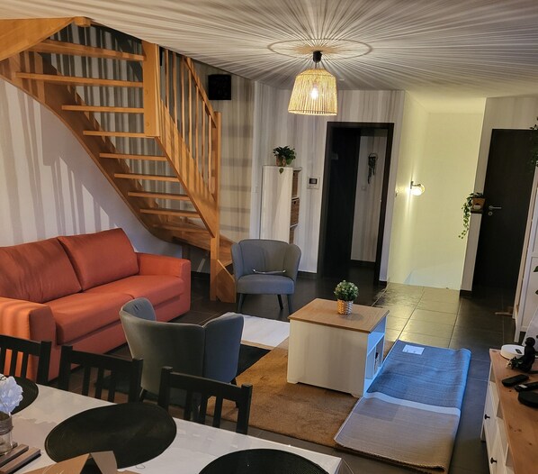 Un salon avec un escalier en bois, un canapé rouge, un fauteuil gris, une table basse et un téléviseur.