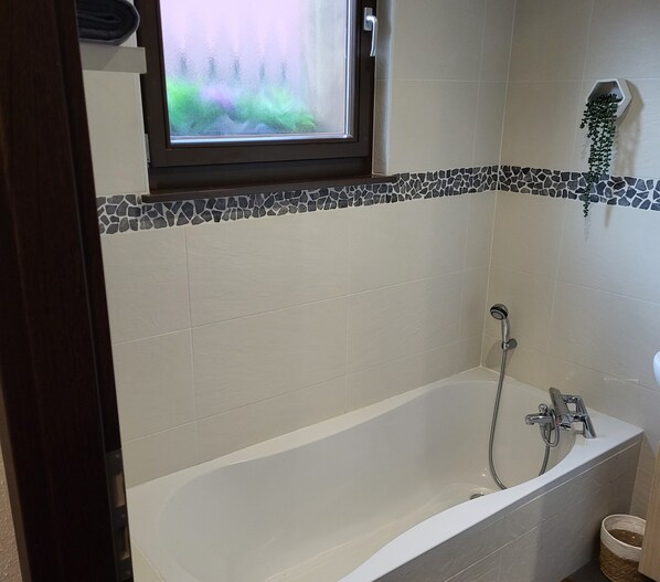 A bathroom with a bathtub, a window, and a tiled wall.