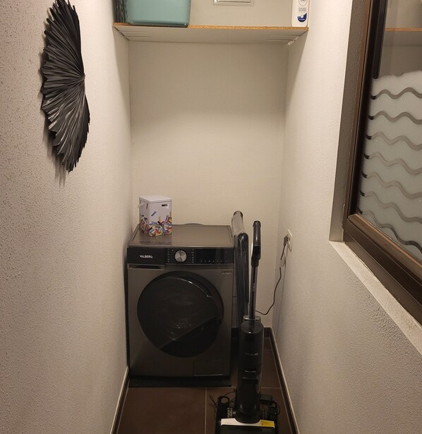 A compact laundry area with a front-loading washing machine, a drying machine, and a vacuum cleaner.