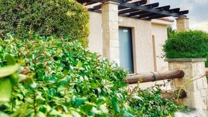 Una casa moderna de dos pisos con techo plano, una pérgola con vigas de madera y un jardín cuidado con arbustos verdes.