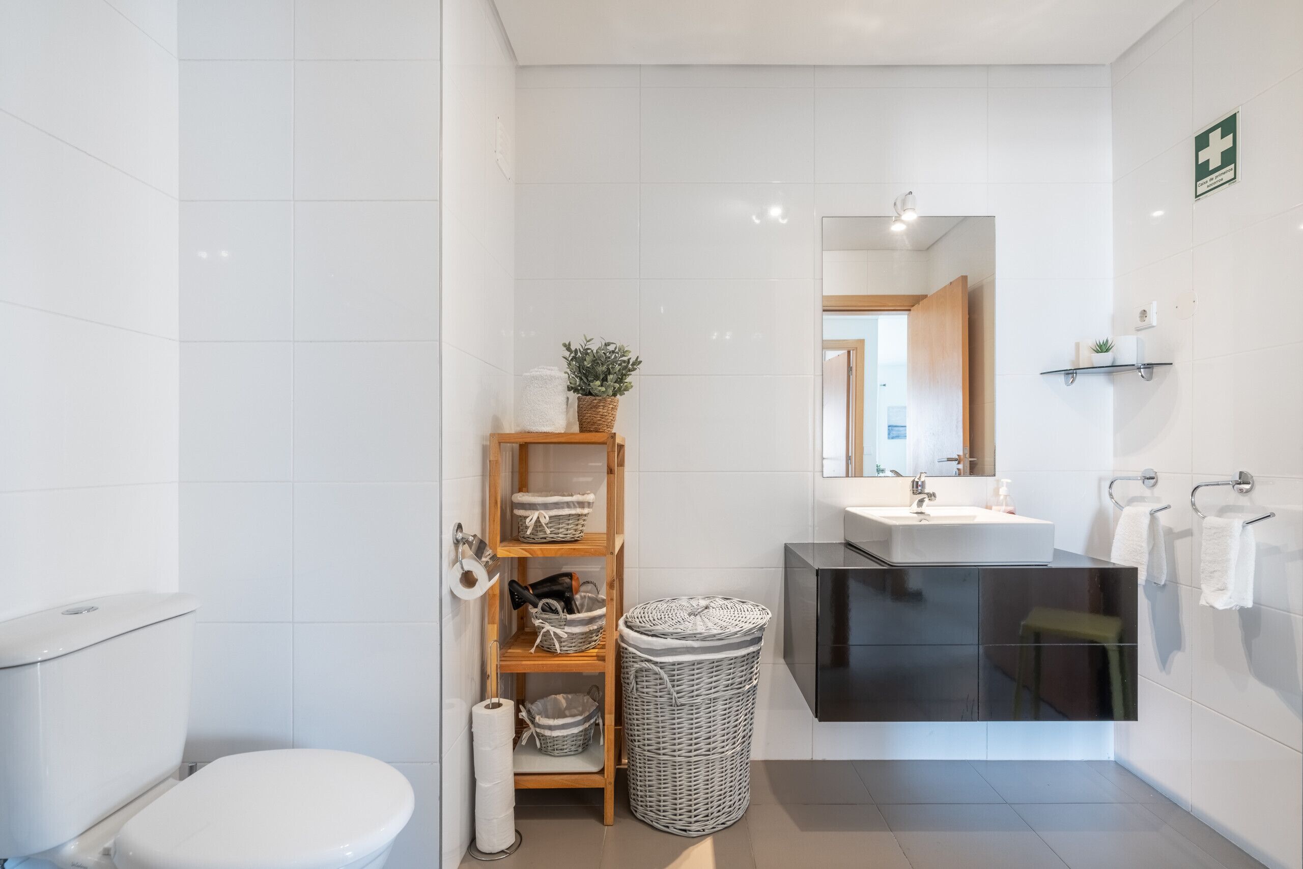 Un baño moderno con inodoro, lavabo, espejo, repisas con cestas y un cubo de basura.