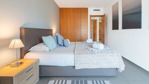 A modern bedroom with a bed, bedside table, and a view of the hallway. - Praia DA Rocha Ocean View by Homing (Portimão)