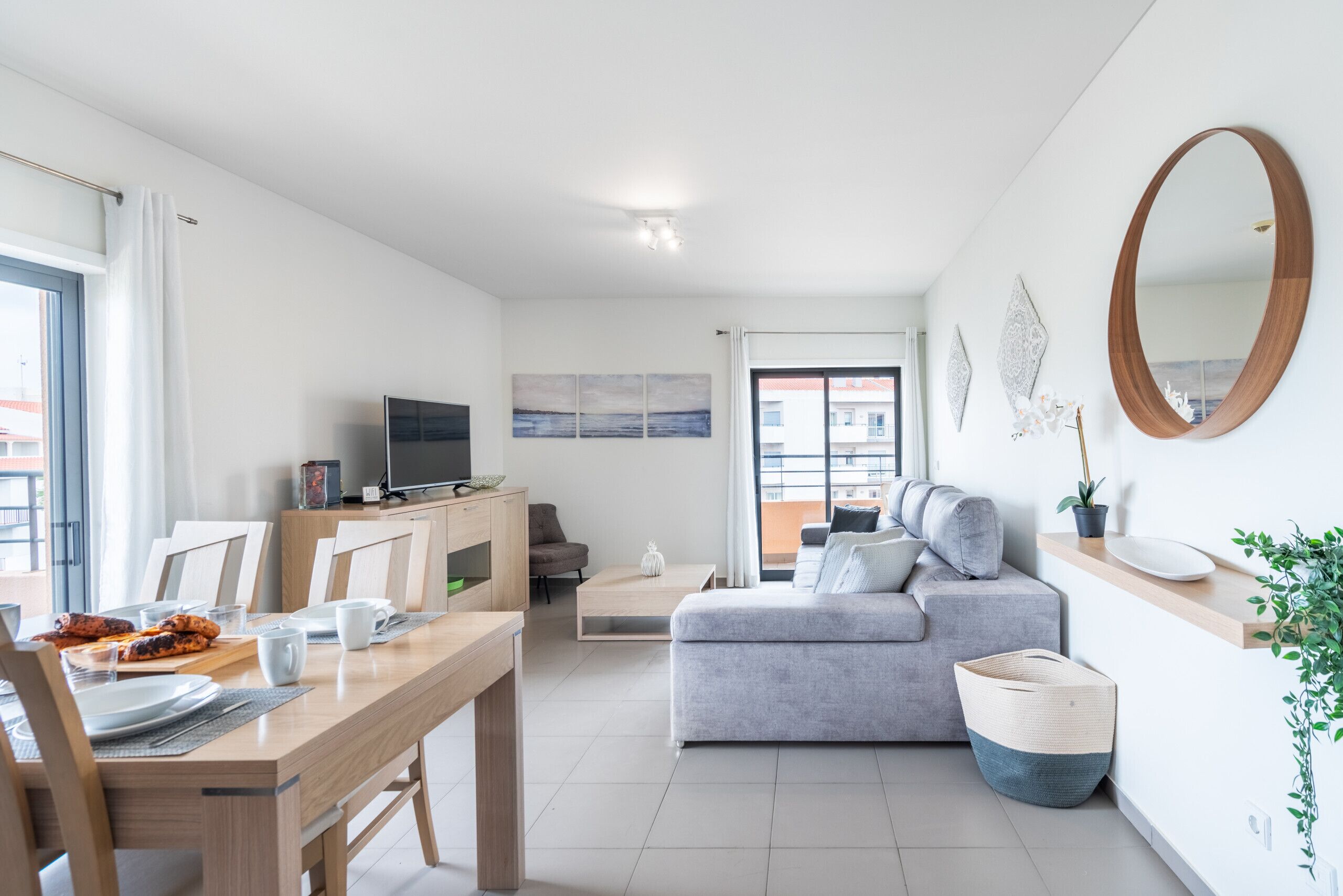 A modern living room with a grey sofa, wooden dining table, and a TV on a cabinet.
