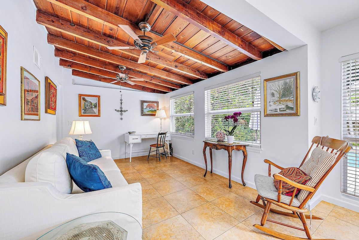 A room with a white sofa, a rocking chair, a desk with a lamp, and a ceiling fan.