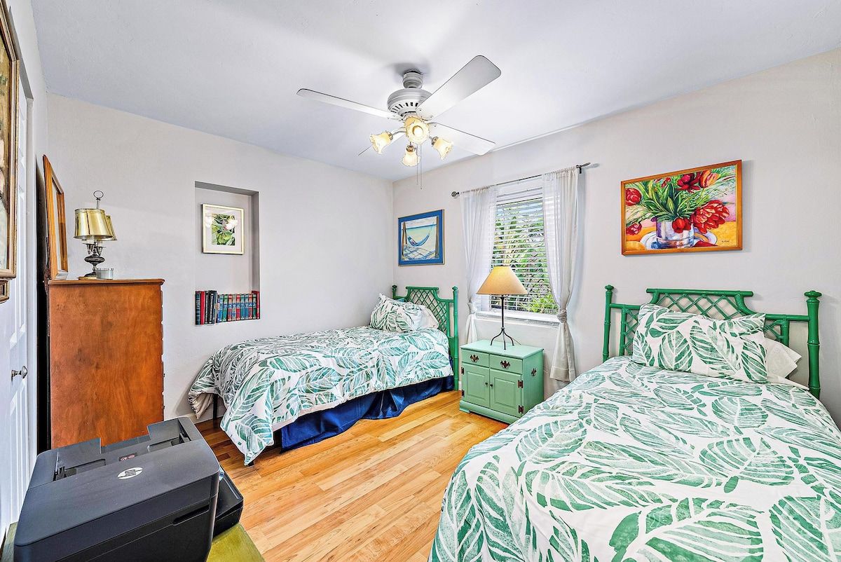 A bedroom with two beds, a ceiling fan, a desk, and a printer.
