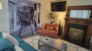 A living room with a sofa, a coffee table, a fireplace, and a large abstract painting on the wall. - Executive Mining House Near MTU (Houghton)