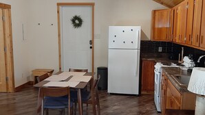 Eine kleine Küche mit Holzausstattung, einem weißen Kühlschrank und einem Essbereich mit Tisch und Stühlen.