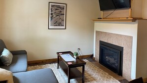 Ein Wohnzimmer mit Kamin, einem an einem Holzbalken befestigten Fernseher und einem gerahmten Kunstwerk an der Wand.