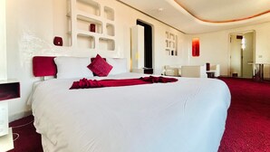 Quarto de hotel moderno com cama grande, parede em destaque vermelha e design minimalista.