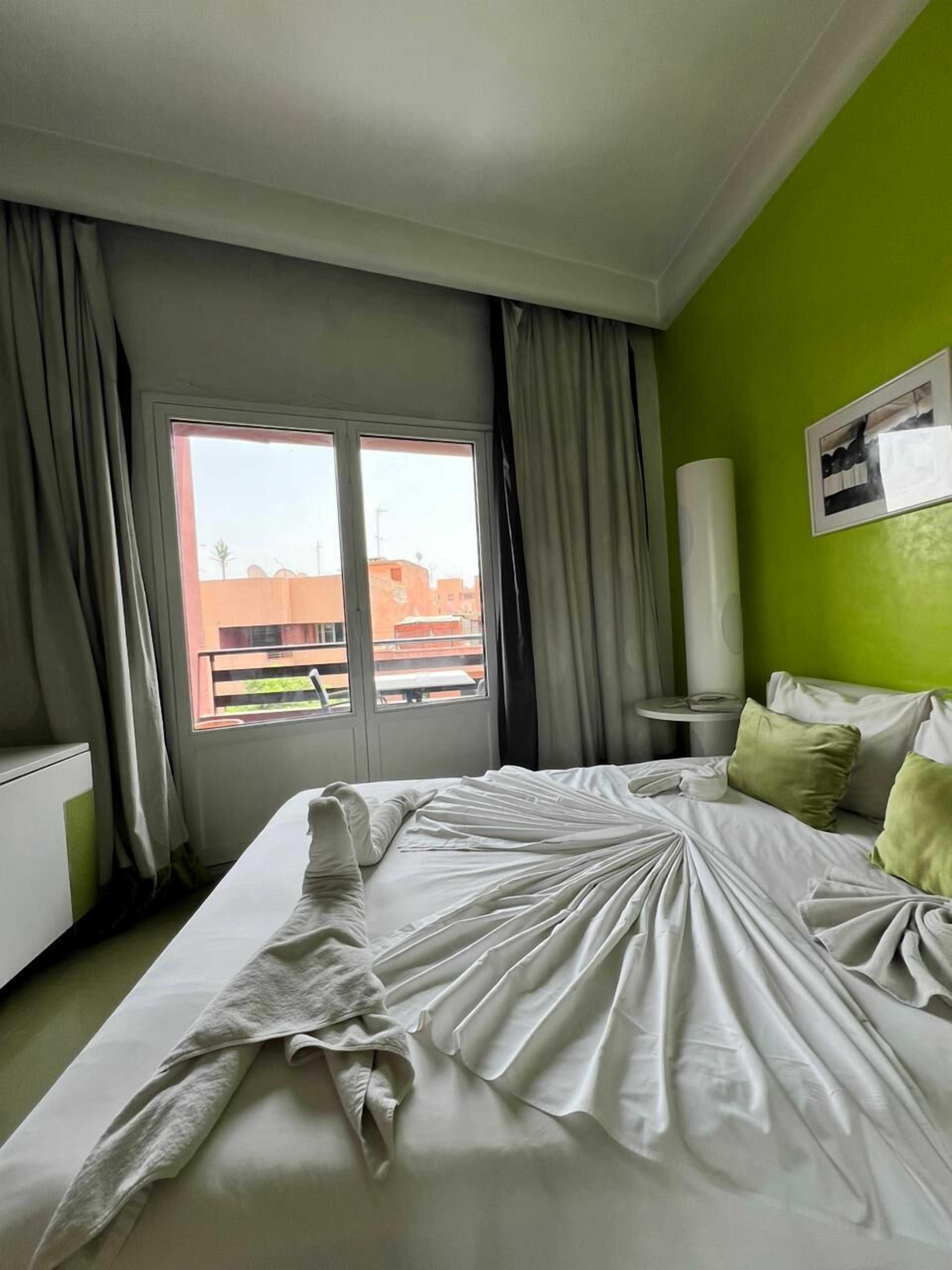 Una habitación de hotel con una cama, una mesita de noche, una ventana con cortinas y una pared verde.