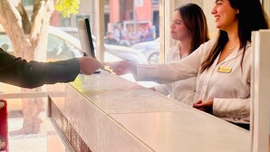 Bancada de recepção com divisória de vidro, uma árvore lá fora e um edifício ao fundo.