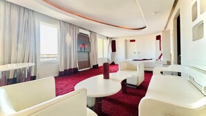 Quarto de hotel moderno com carpete vermelho, mobiliário branco, televisão e uma porta.