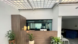 A reception area with a wooden reception desk, a large window, and potted plants. - Outlanders House (Bogota)