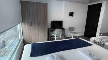 Habitació d'hotel amb llit, escriptori, cadira, televisió i armari.