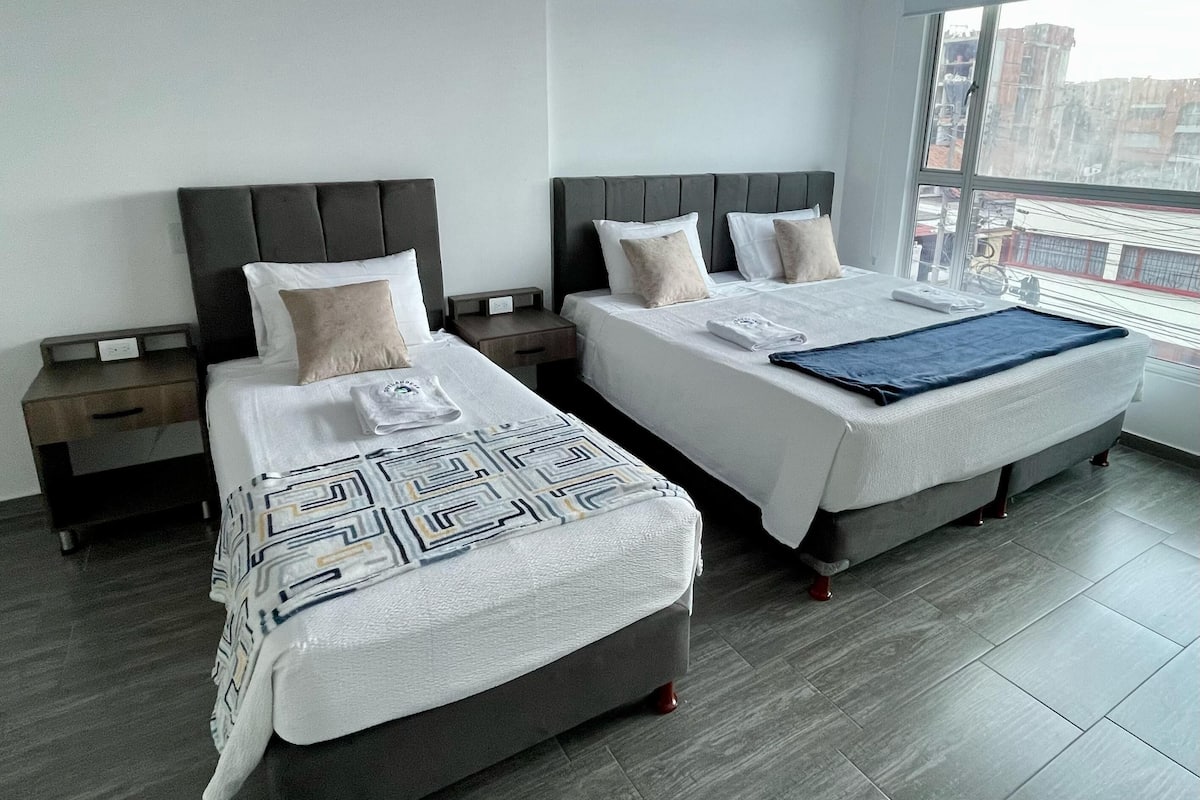 Una habitación de hotel moderna con dos camas, un ventanal grande y vistas a la ciudad.