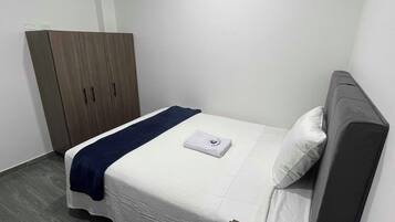 A small, neatly arranged bedroom with a bed, a wardrobe, and a nightstand.