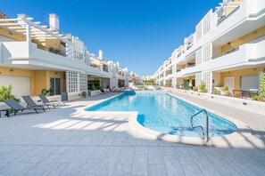 A modern hotel with a central swimming pool, sun loungers, and balconies.