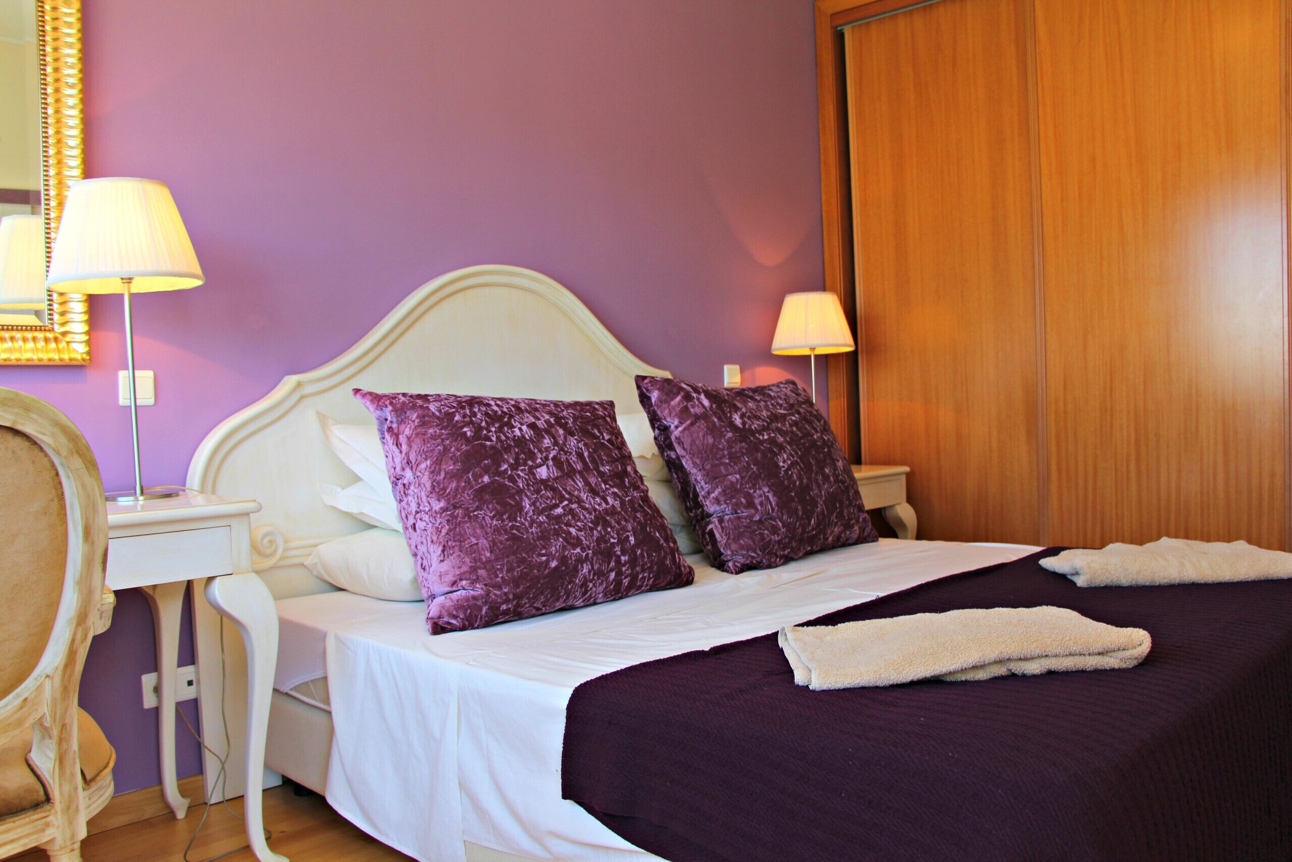 A bedroom with a bed, two lamps, a nightstand, and a wooden door.
