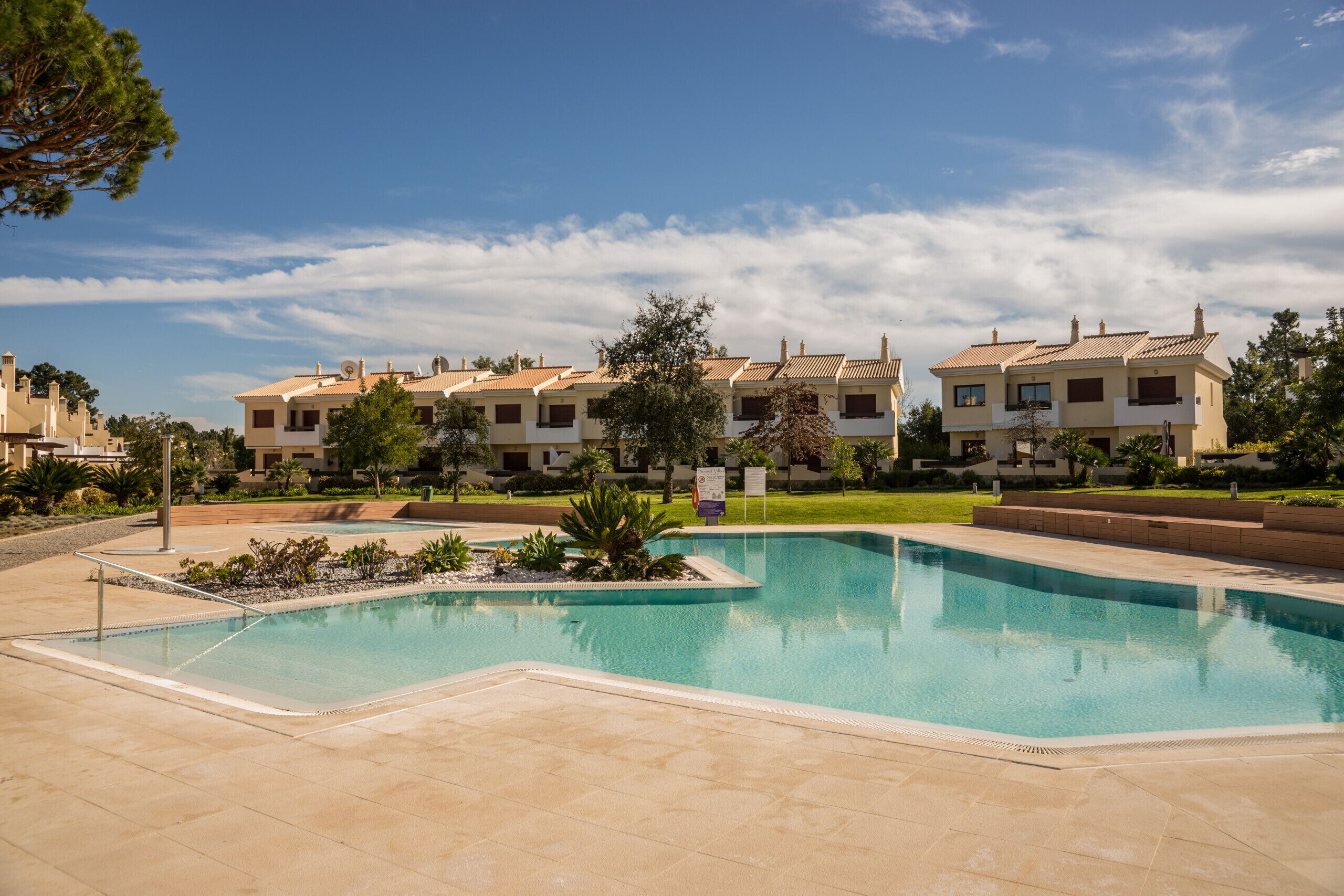 A swimming pool surrounded by a landscaped area with a row of residential buildings in the background.