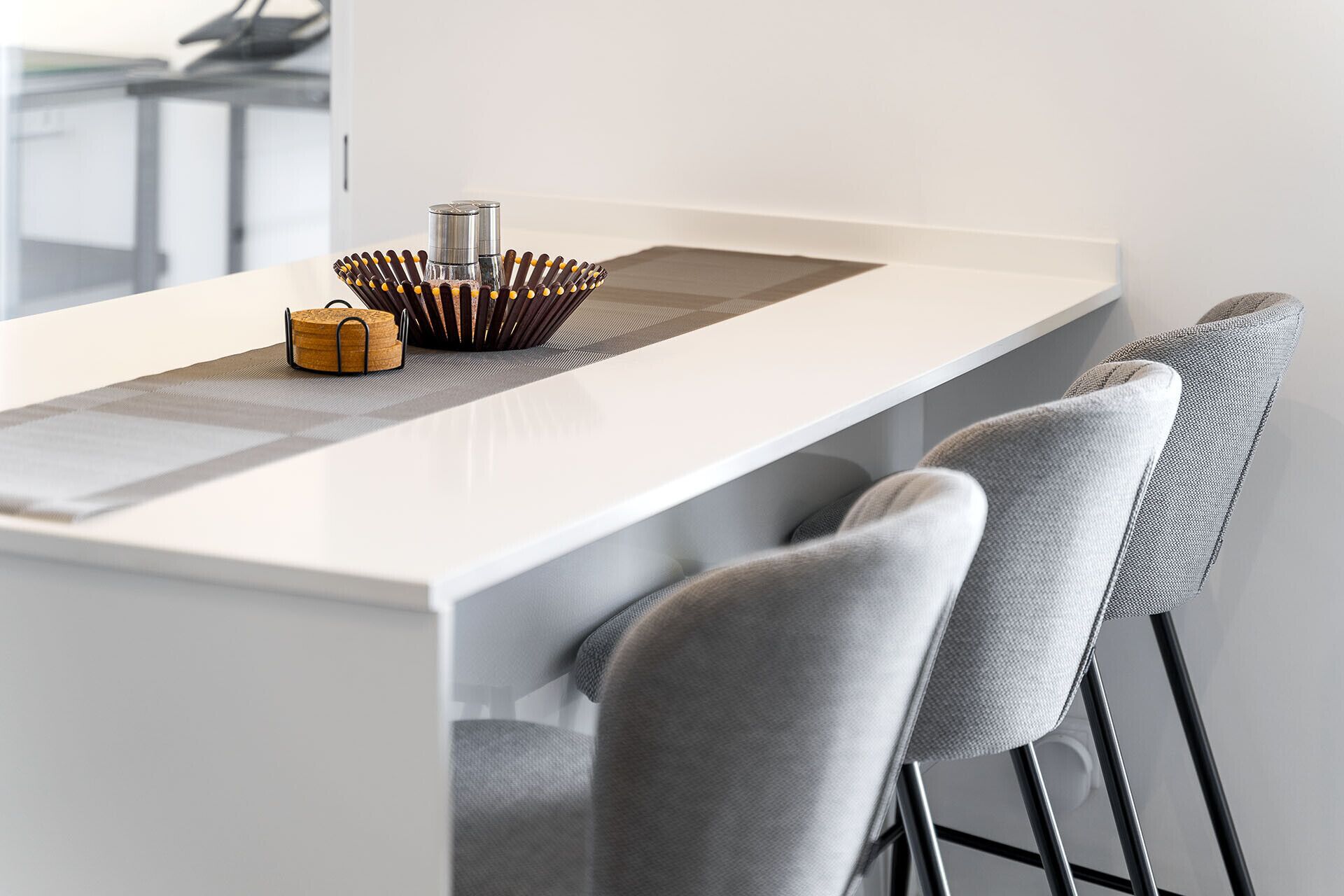 Une cuisine moderne avec un plan de travail blanc, une bouilloire en acier inoxydable et un sous-verre en liège.