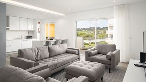 A modern living room with a grey sofa set, a small armchair, and a flat-screen TV. The room features a large window with a view of a residential area. - Lagos Modern 1 With Pool by Homing (Lagos)